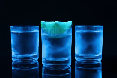Photo of Shot glasses of vodka with lime slice on dark background