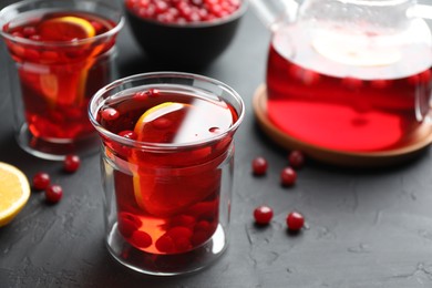 Photo of Tasty hot cranberry tea with lemon and fresh berries in glass on black textured table