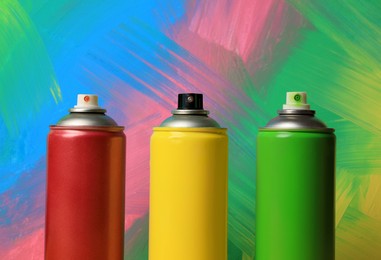 Photo of Cans of different spray paints on color background, closeup. Graffiti supplies