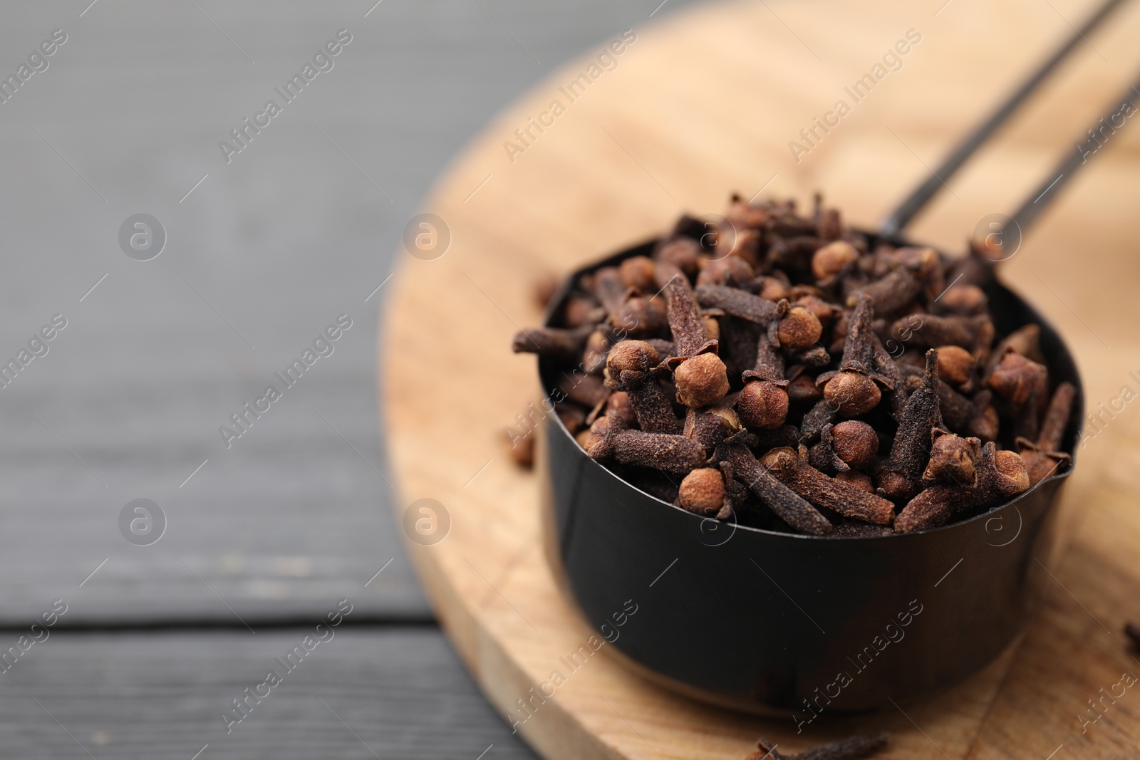 Photo of Aromatic cloves in scoop on grey wooden table, closeup. Space for text