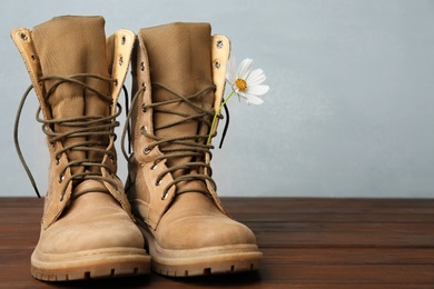 Photo of Military boots with flower on wooden surface, space for text. Armed Forces Day