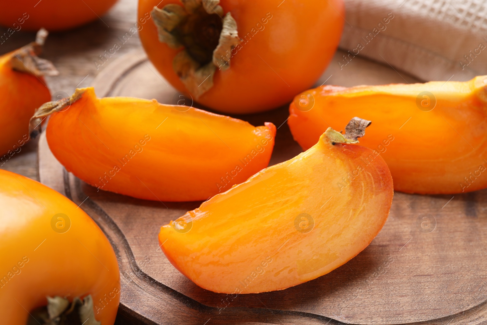 Photo of Whole and cut delicious ripe persimmons on wooden table, closeup