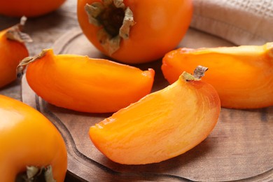 Whole and cut delicious ripe persimmons on wooden table, closeup