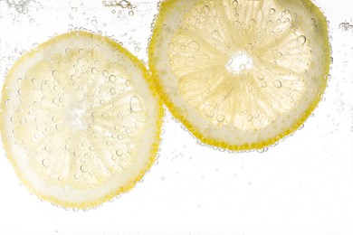 Juicy lemon slices in soda water against white background, closeup