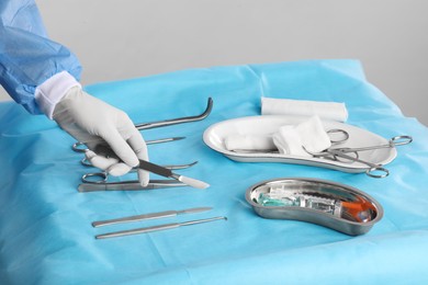 Photo of Doctor holding scalpel over table with surgical instruments against light background, closeup
