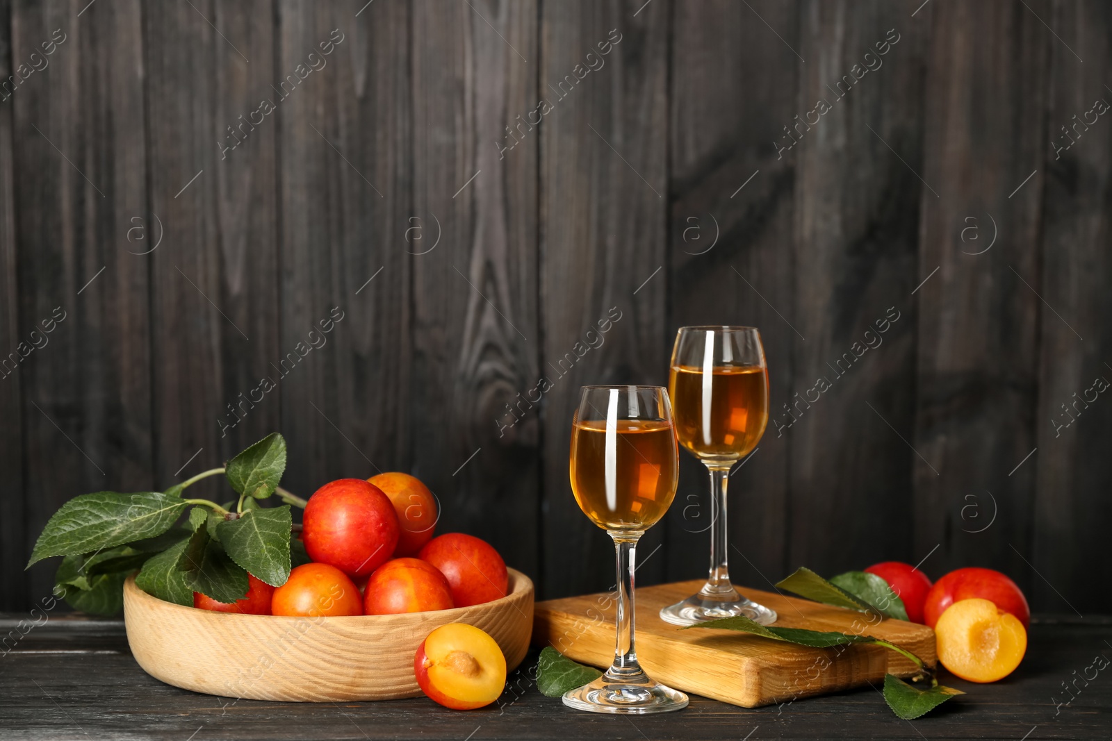 Photo of Delicious plum liquor and ripe fruits on black wooden table. Homemade strong alcoholic beverage