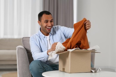 Photo of Happy young man opening parcel at home. Internet shopping