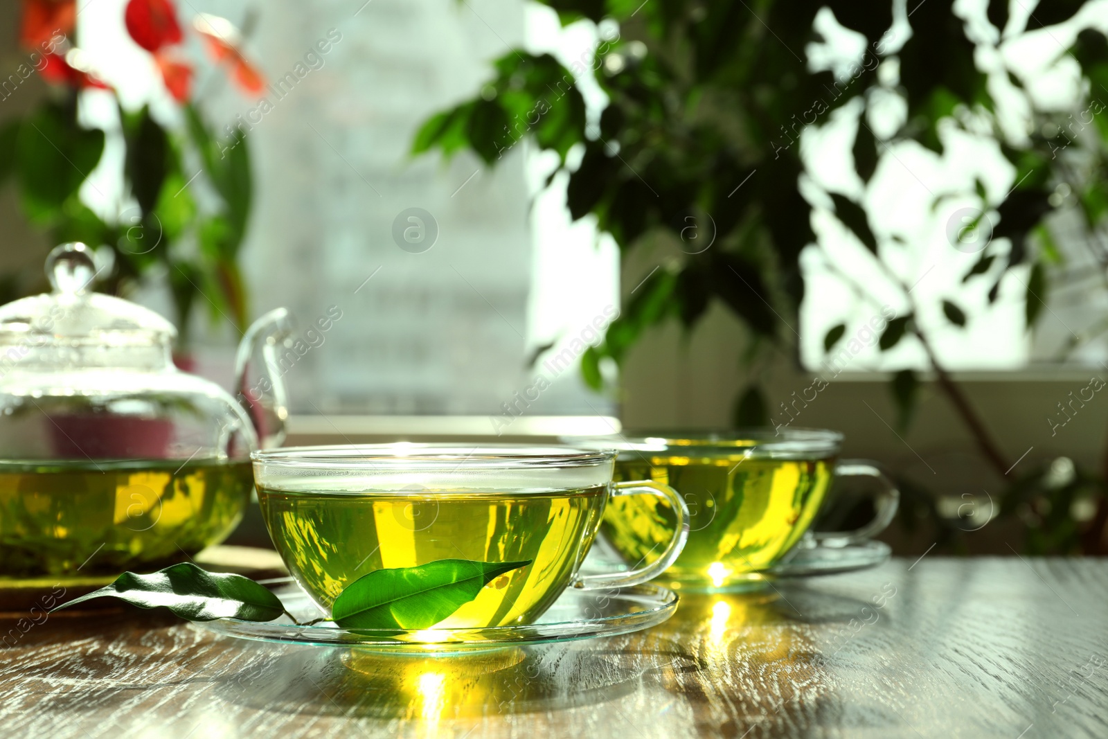 Photo of Fresh green tea in glass cups, leaves and teapot on wooden table