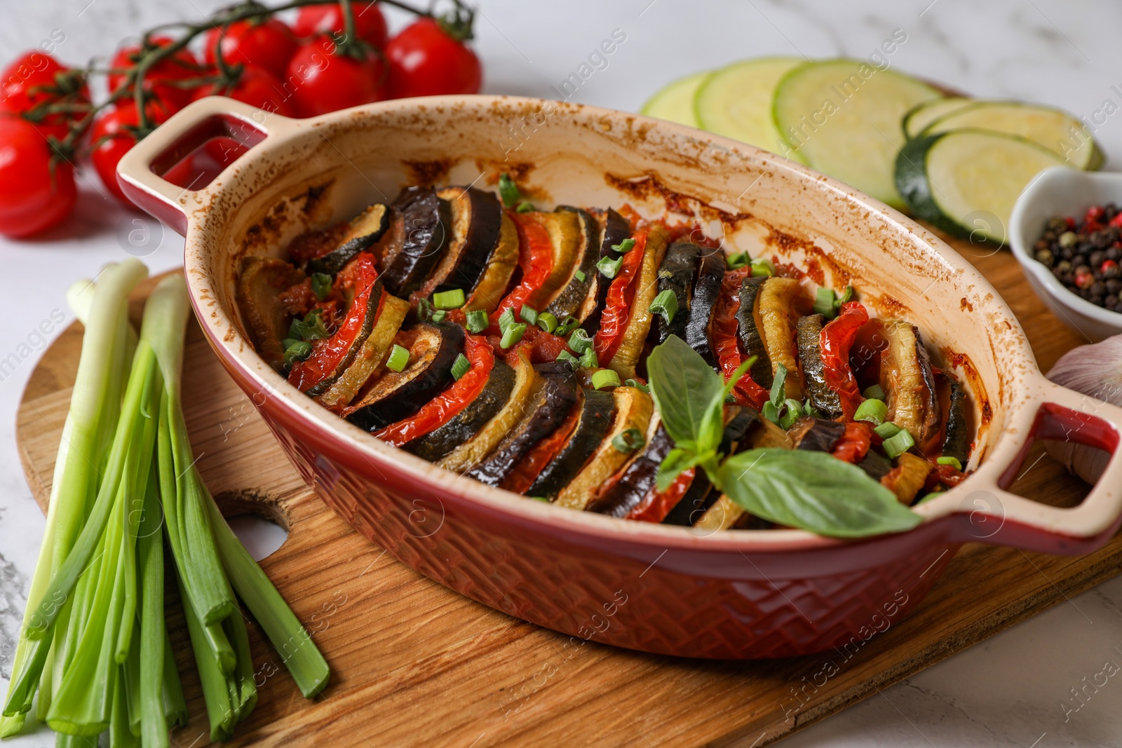 Photo of Delicious ratatouille in dish and ingredients on table