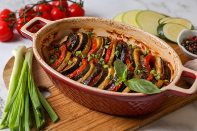 Photo of Delicious ratatouille in dish and ingredients on table