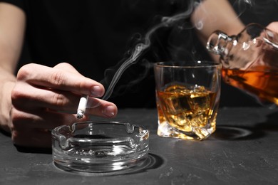 Photo of Alcohol addiction. Man with smoldering cigarette pouring whiskey into glass at dark textured table, closeup