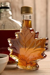 Photo of Bottles and bowl of tasty maple syrup on wooden table, closeup