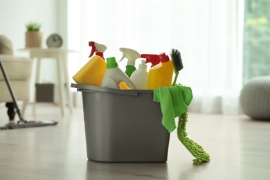 Photo of Bucket with different cleaning supplies on floor indoors