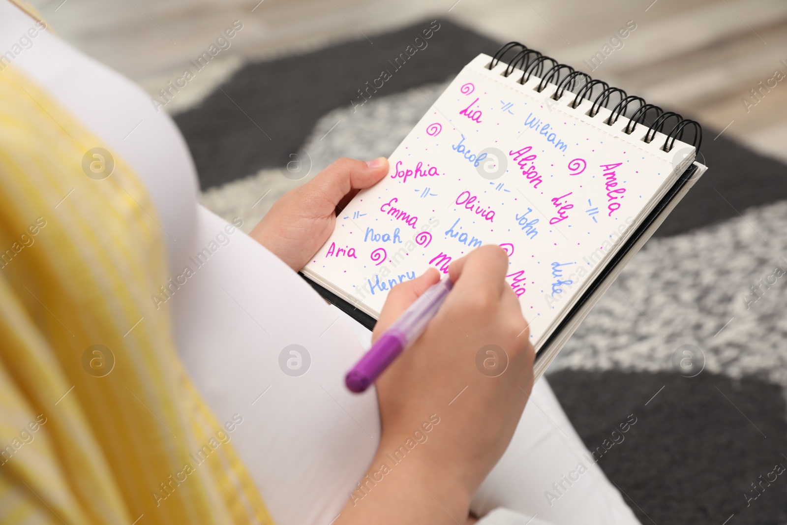 Photo of Pregnant woman with baby names list sitting on floor, closeup