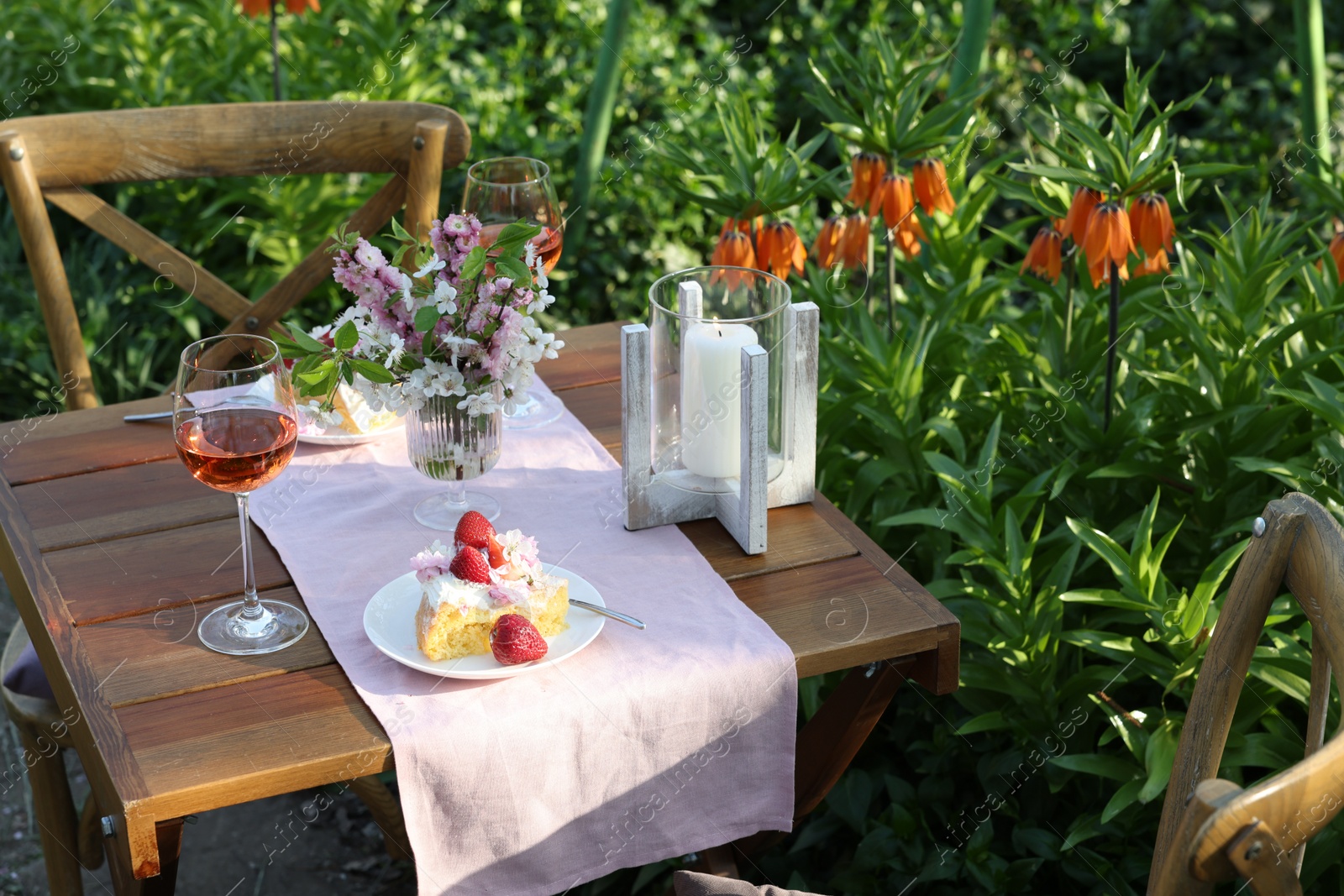 Photo of Vase with spring flowers, wine and cake on table served for romantic date in garden