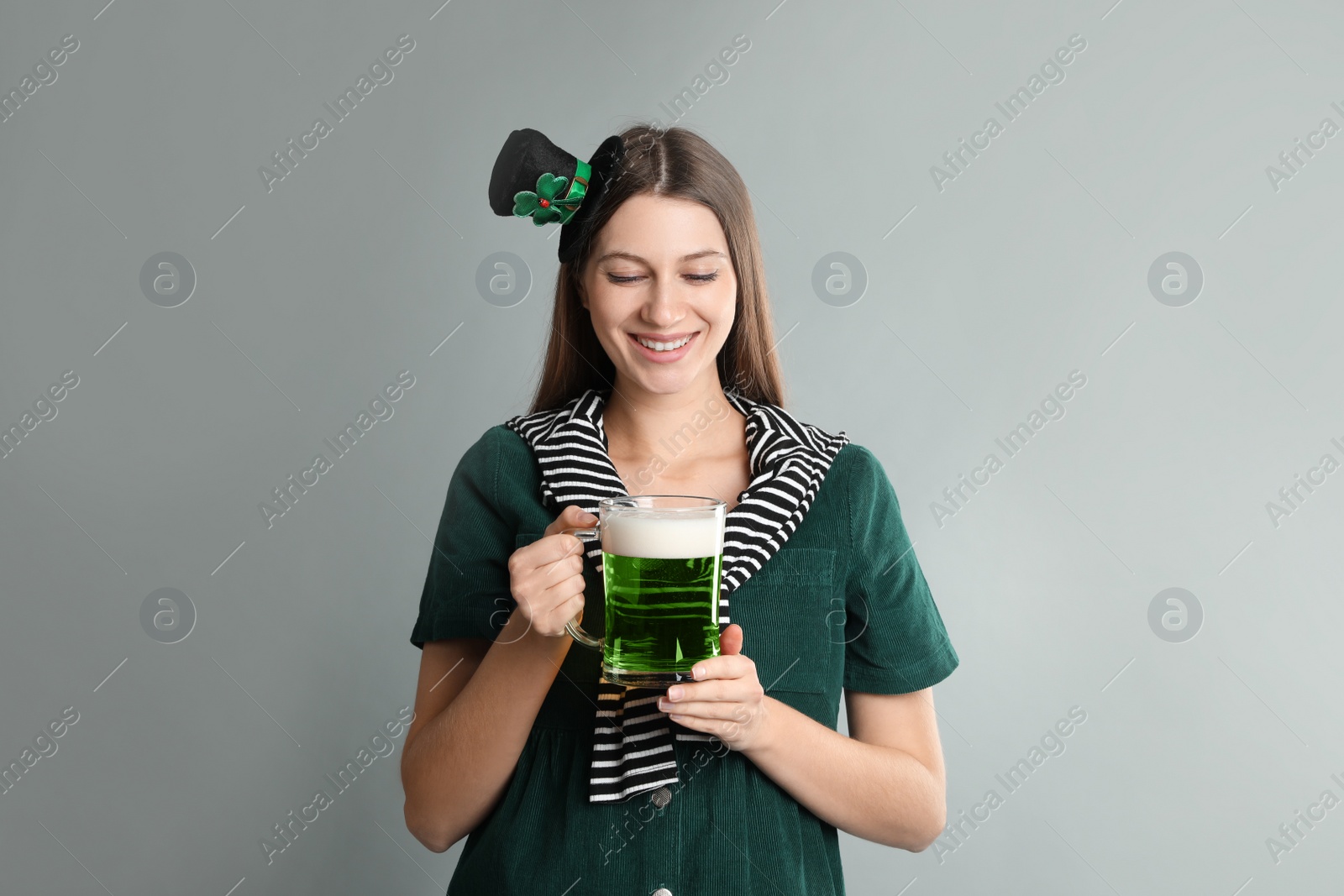 Photo of Happy woman in St Patrick's Day outfit with beer on light grey background