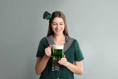 Happy woman in St Patrick's Day outfit with beer on light grey background