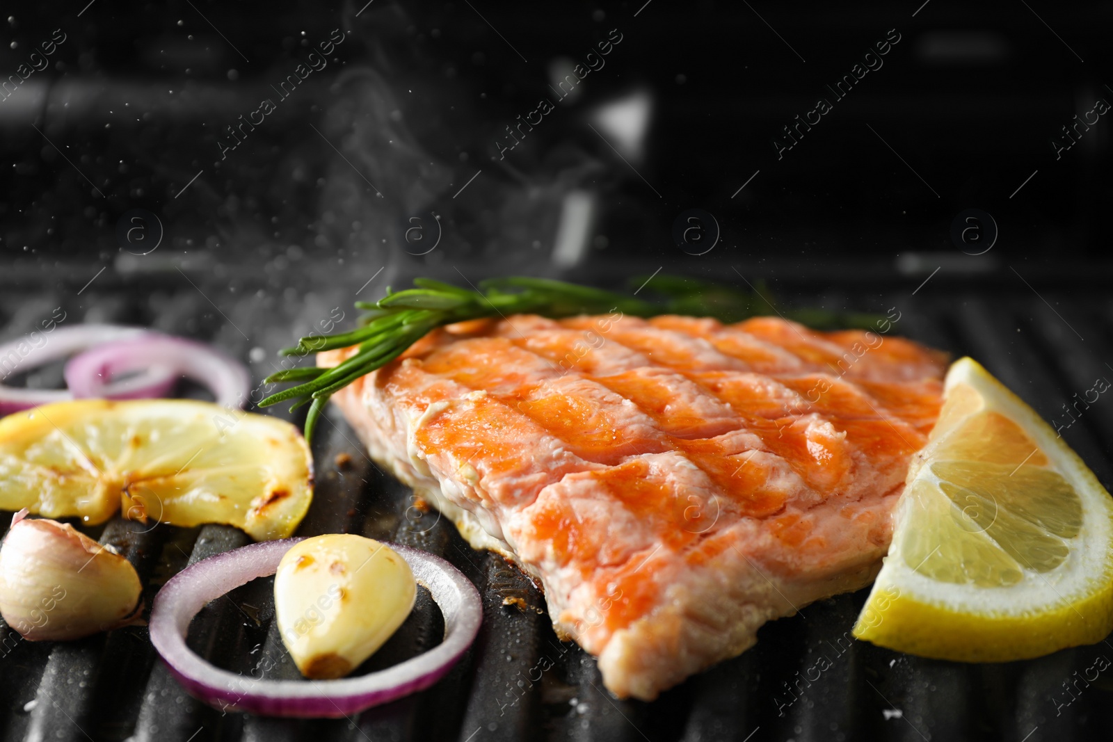 Photo of Tasty salmon cooking with rosemary, garlic, onion and lemon on electric grill, closeup