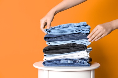 Photo of Woman arranging stack of different jeans on table against color background