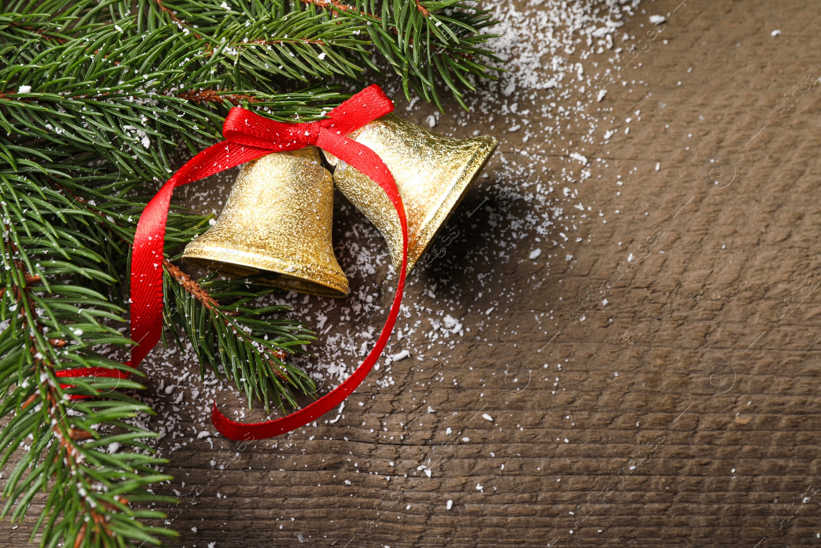 Photo of Christmas bells and fir tree branches on wooden table, flat lay. Space for text