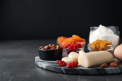 Photo of Marzipan and other ingredients for homemade Stollen on grey table against dark background. Baking traditional German Christmas bread