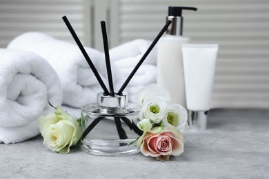 Photo of Towels, reed air freshener, cosmetic products and flowers on grey table indoors