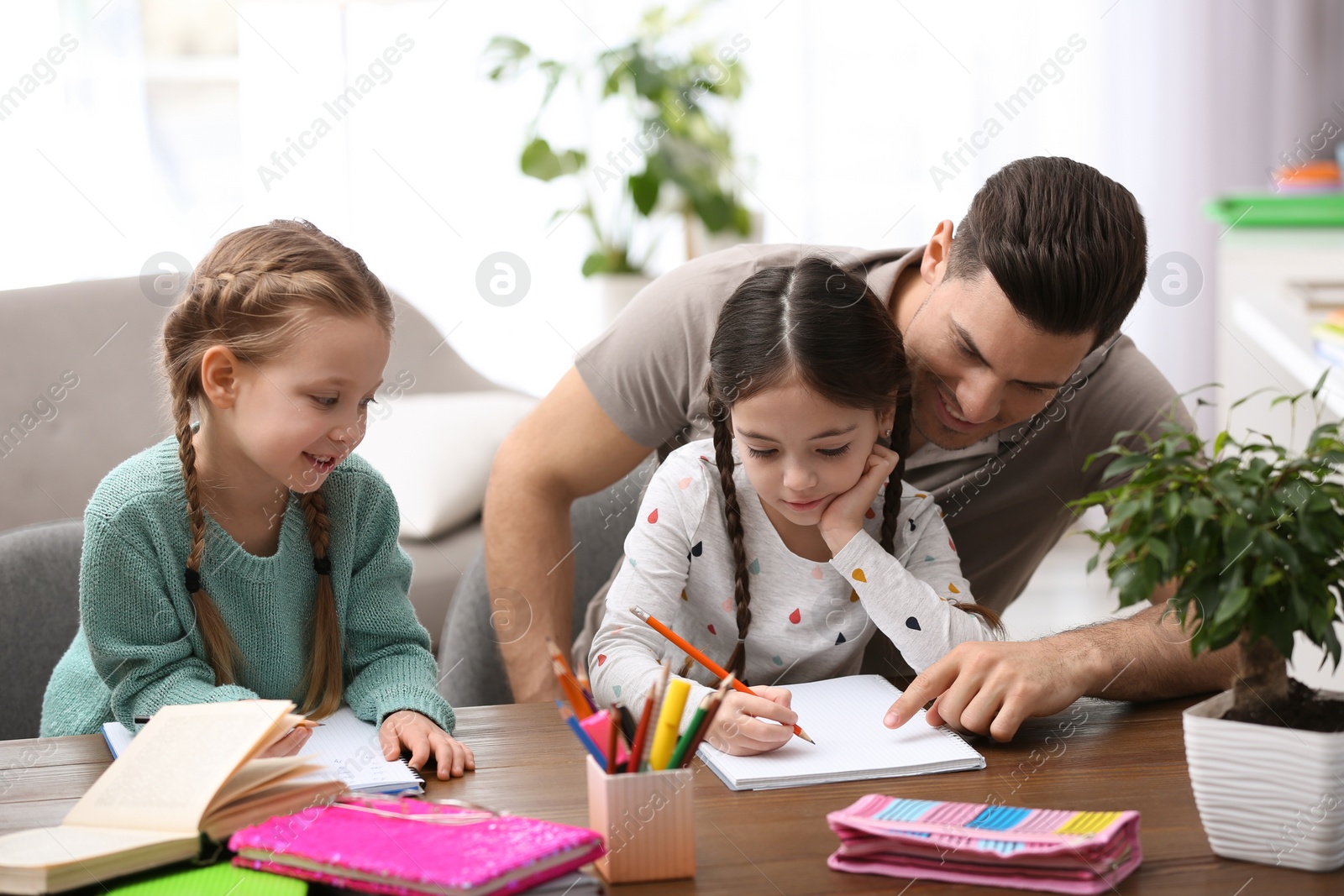 Photo of Father helping his daughters with homework at table indoors