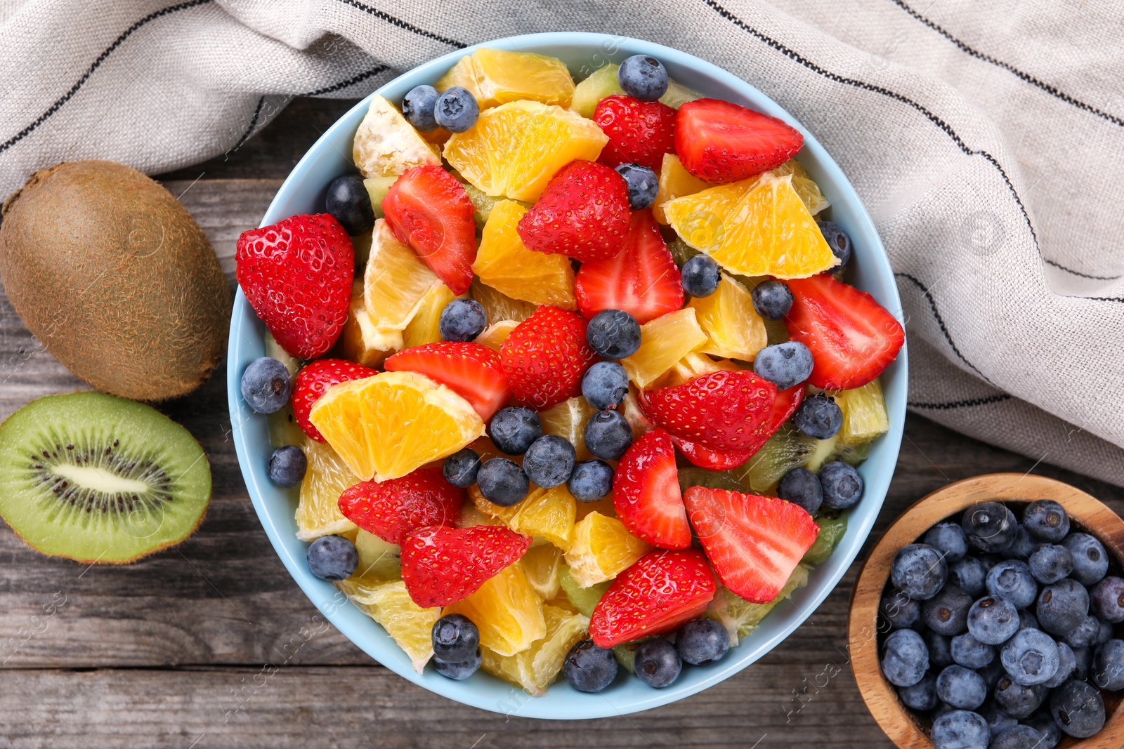 Delicious fresh fruit salad and ingredients in bowl on wooden table, flat lay Photo of Delicious fresh fruit salad and ingredients in bowl on wooden table, flat lay