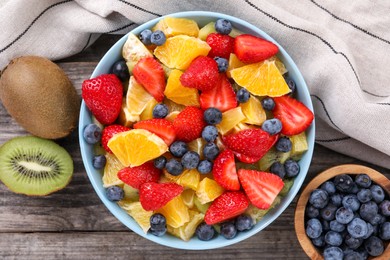 Photo of Delicious fresh fruit salad and ingredients in bowl on wooden table, flat lay