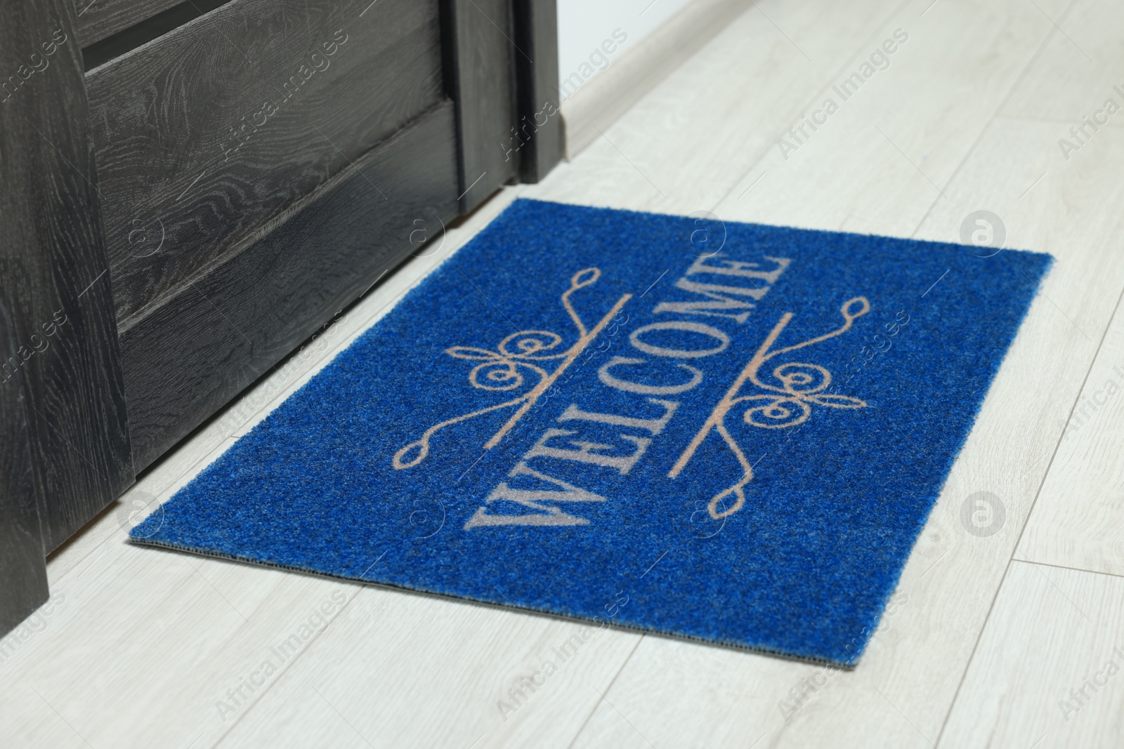 Photo of Blue doormat with word Welcome on white floor near entrance