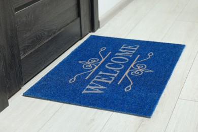 Photo of Blue doormat with word Welcome on white floor near entrance