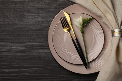 Stylish table setting. Plates, cutlery, napkin and floral decor on dark wooden background, top view with space for text