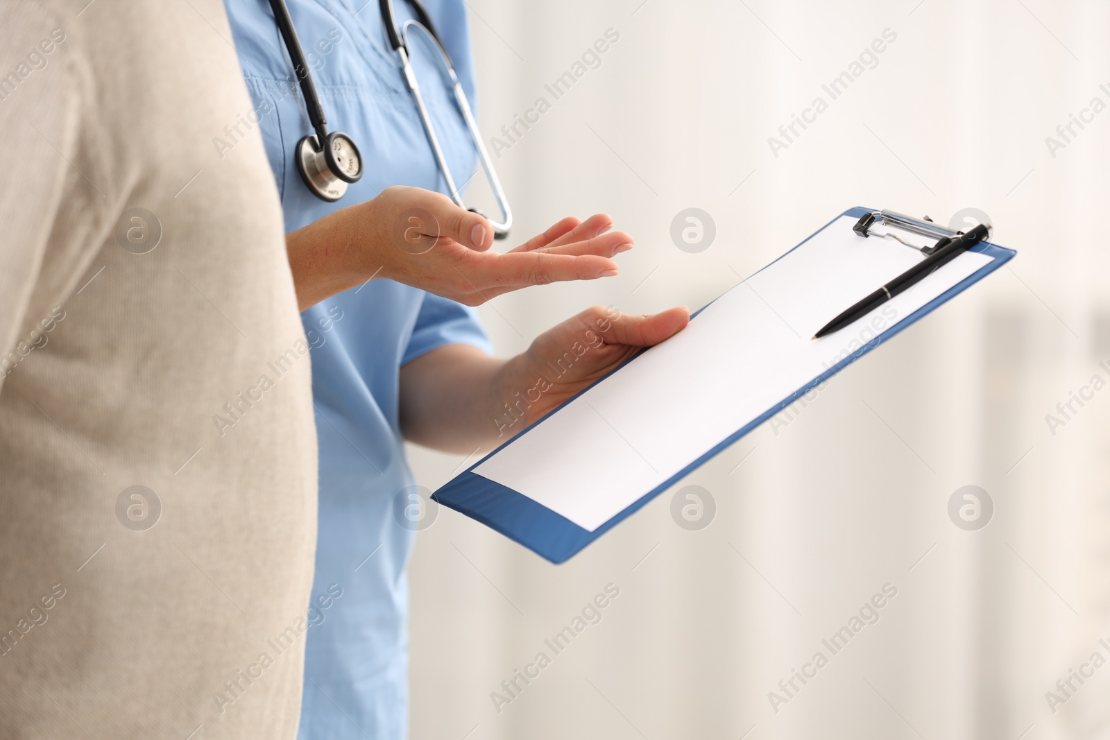 Photo of Nurse with clipboard and elderly patient indoors, closeup