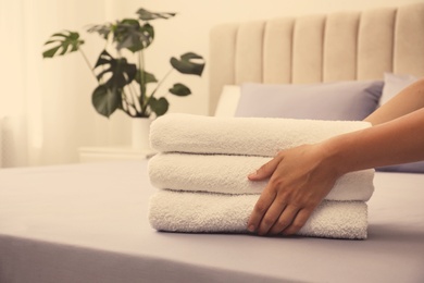 Photo of Woman putting Soft clean terry towels on bed, closeup