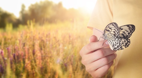 Image of Woman holding beautiful rice paper butterfly in sunlit field, closeup