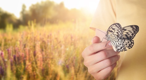 Woman holding beautiful rice paper butterfly in sunlit field, closeup