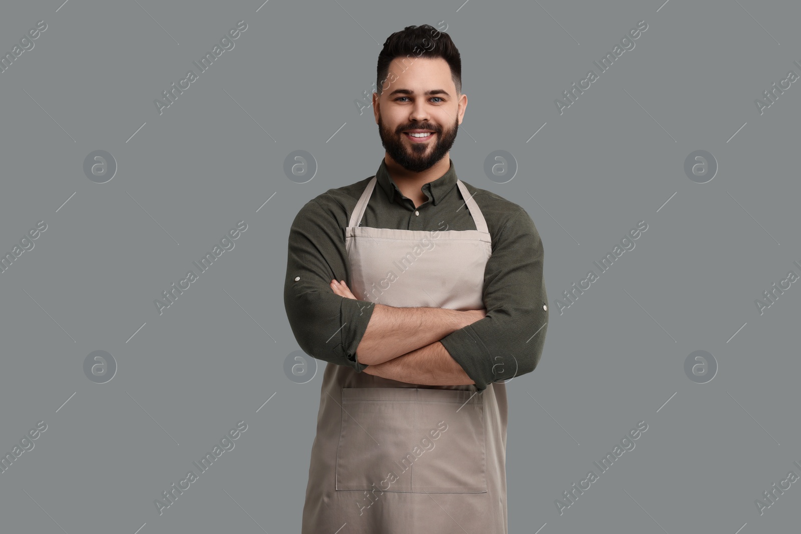 Photo of Smiling man in kitchen apron with crossed arms on grey background. Mockup for design