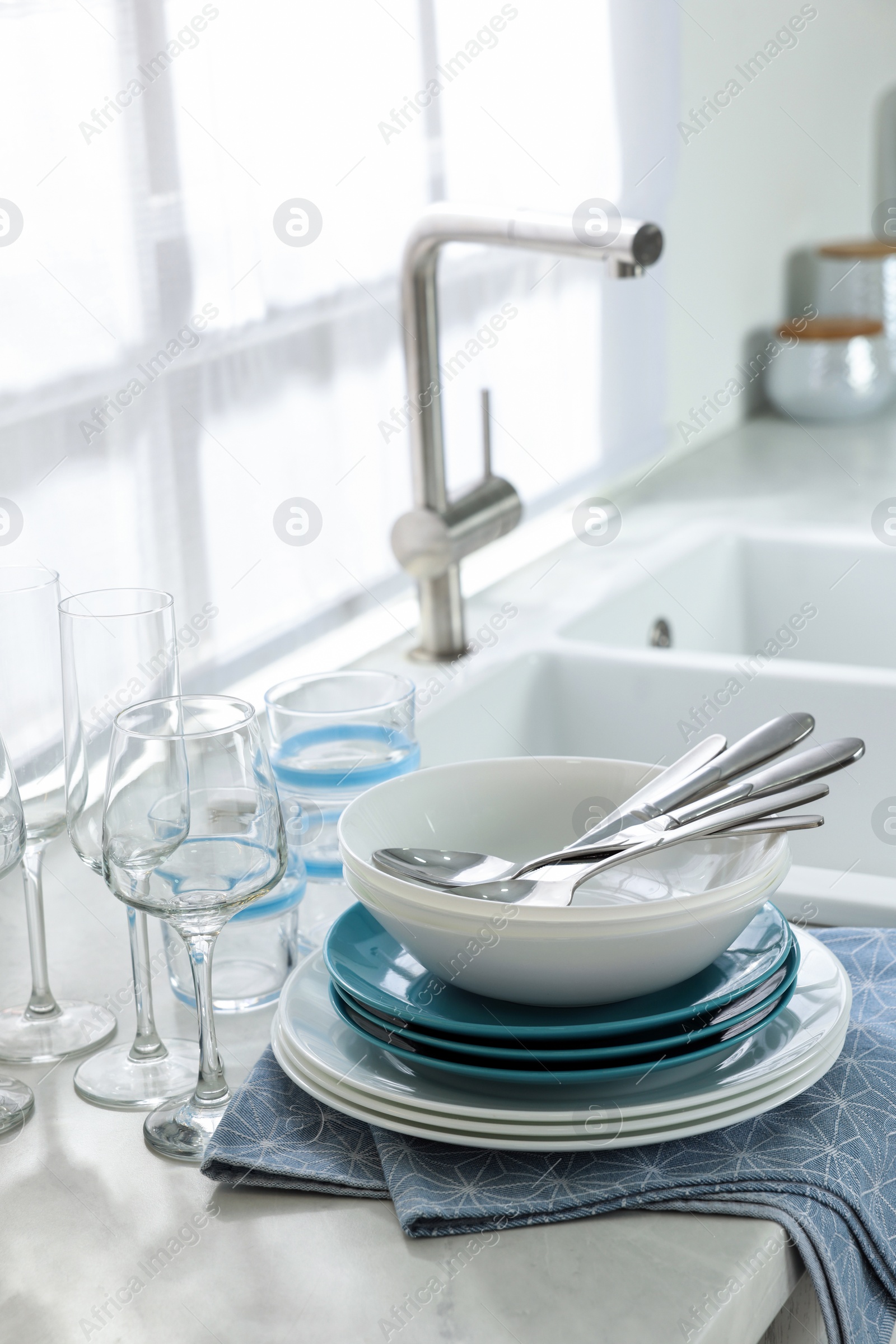 Photo of Different clean dishware, cutlery and glasses on countertop in kitchen