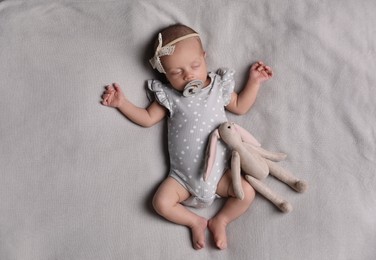 Photo of Adorable newborn baby with pacifier and toy bunny sleeping on bed, top view