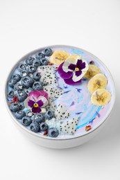 Delicious smoothie bowl with fresh fruits, blueberries and flowers on white background