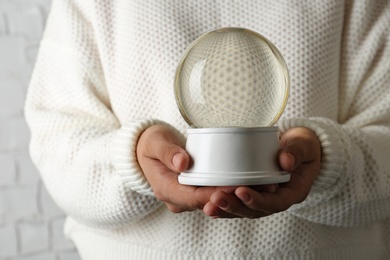 Photo of Woman wearing white sweater holding empty snow globe, closeup