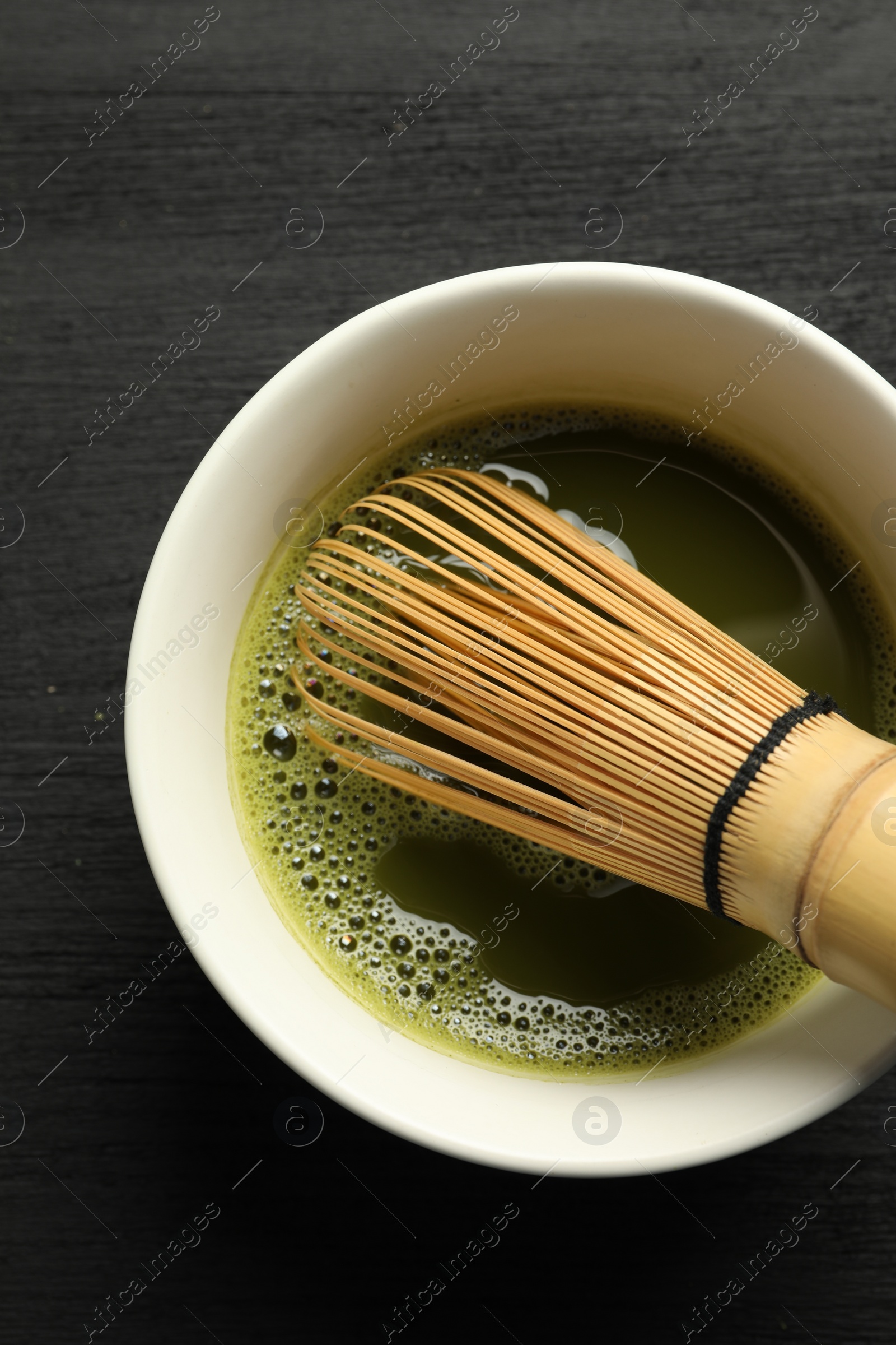 Photo of Cup of fresh matcha tea with bamboo whisk on black wooden table, top view