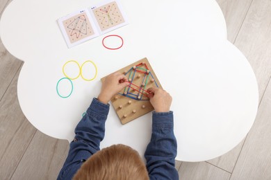 Photo of Motor skills development. Boy playing with geoboard and rubber bands at white table, top view