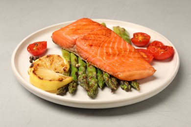 Photo of Tasty grilled salmon with asparagus, tomatoes, spices and lemon on light grey table