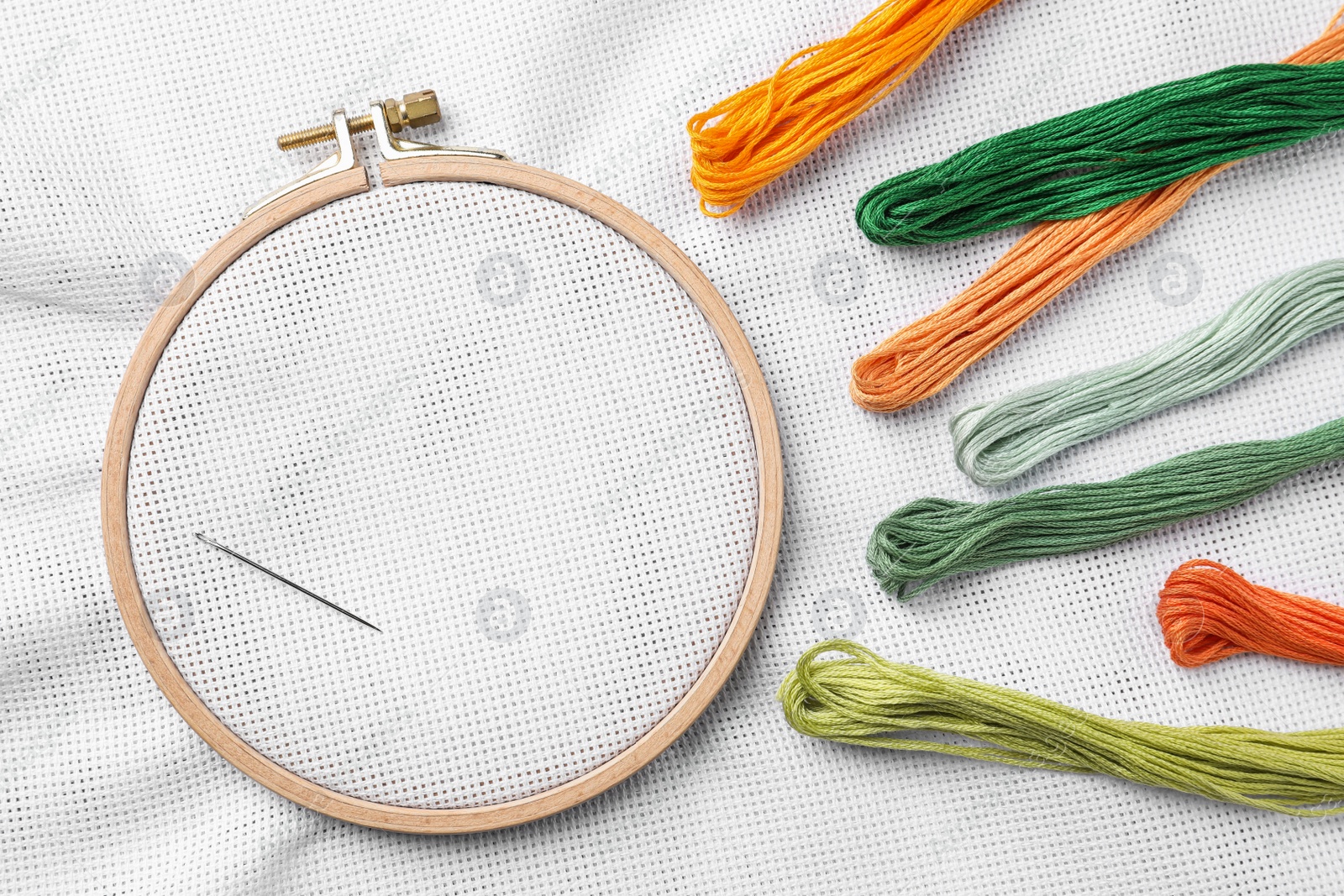 Photo of Threads near embroidery hoop with white fabric, flat lay