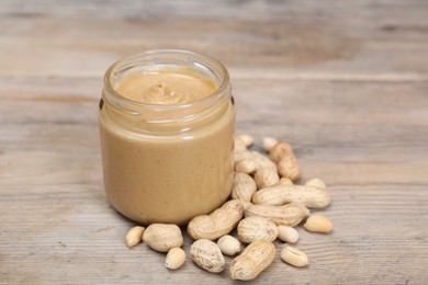 Tasty nut paste in jar and peanuts on wooden table, closeup