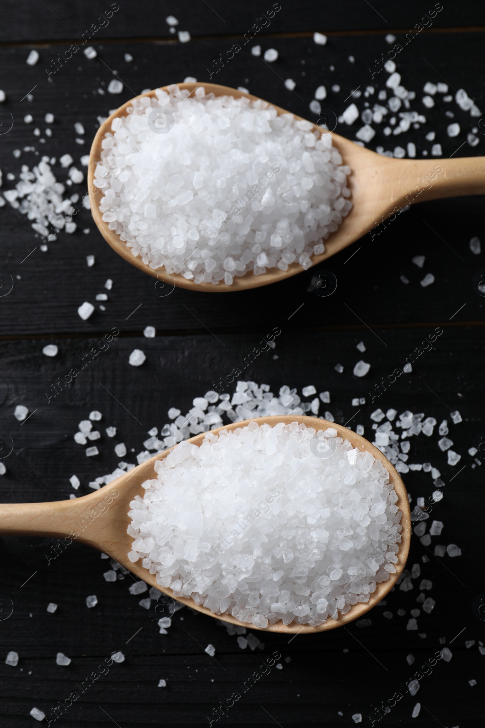 Photo of Organic salt in spoons on black wooden table, top view