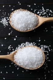 Photo of Organic salt in spoons on black wooden table, top view