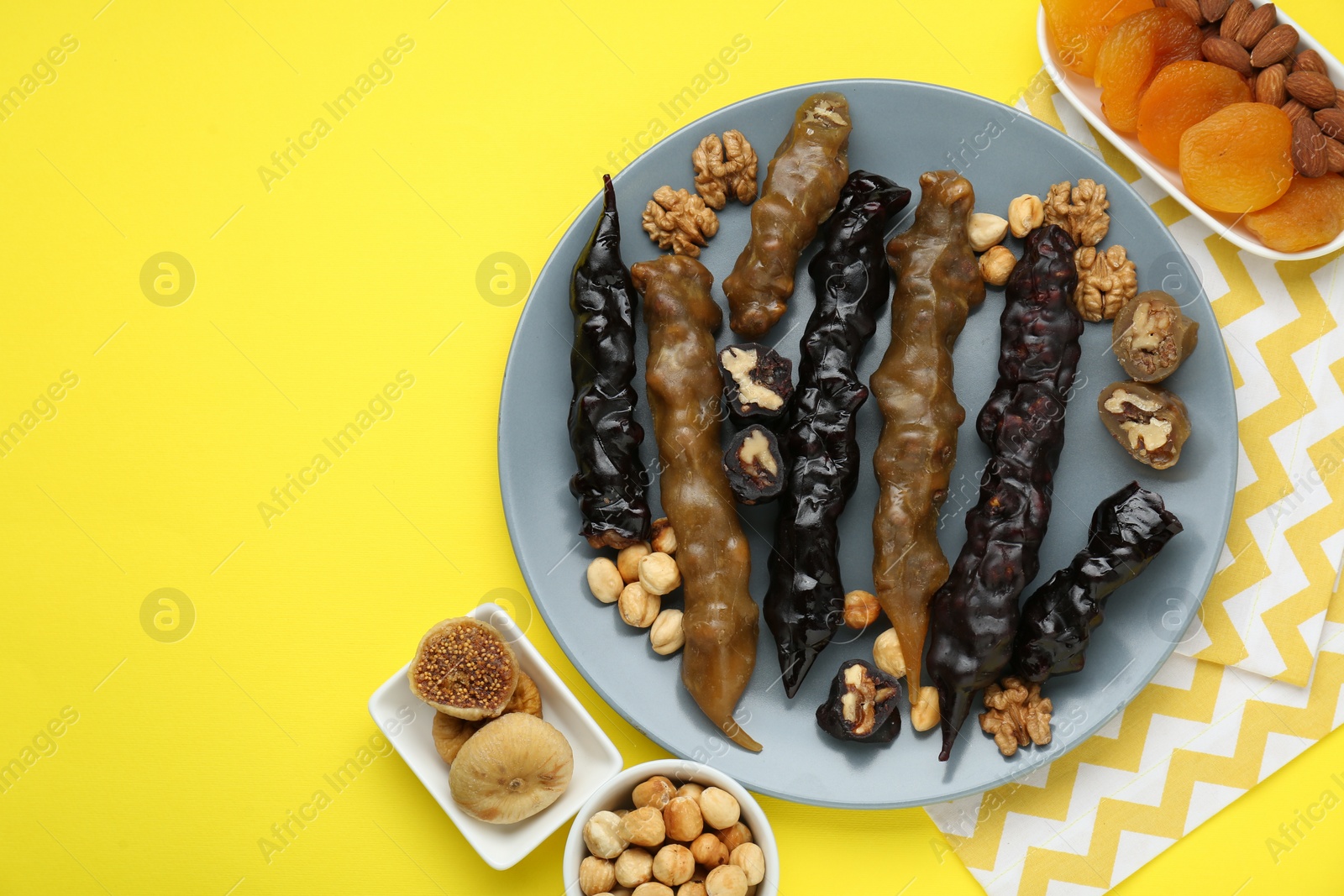 Photo of Plate with delicious churchkhelas, nuts and dried fruits on yellow background, flat lay. Space for text