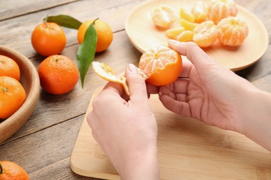 Photo of Woman peeling fresh ripe tangerine at wooden table, closeup